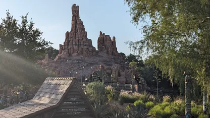 Jagged red rock mountain with a wooden-roofed building and desert plants in the foreground.