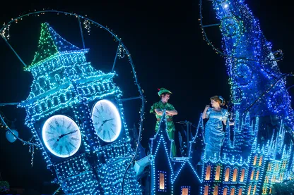 boy in green suit with hat girl in blue dress with blue bow in hair lights all over big ben and top of buildings float parade disney starlight night time show