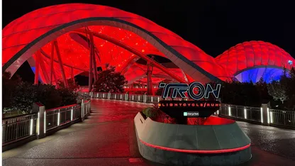 TRON Lightcycle/Run roller coaster entrance beneath a red-lit futuristic canopy at night.