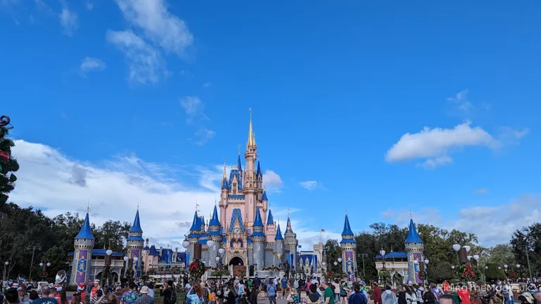 Cinderella Castle at Walt Disney World, with visitors gathered in the foreground under a blue sky.