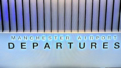 Manchester Airport Departures sign beneath a ribbed ceiling.