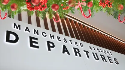 A Christmas tree with ornaments and candy canes hangs above the Manchester Airport Departures sign