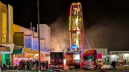 night sky smoke in air 2 US style trucks, a ferris wheel, and people standing by lamp post