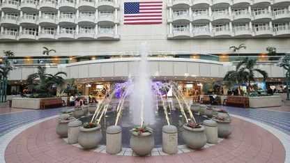 fountain with pots around, tiled floor, american flag on white wall orlando airport