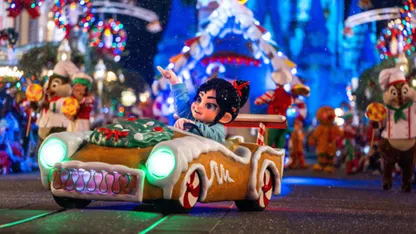 Child character riding a gingerbread-themed car in a colourful Christmas parade.