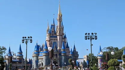 Cinderella Castle at Magic Kingdom, with blue-roofed towers, landscaped gardens and visitors beneath a clear blue sky.