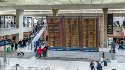 A busy airport with people walking around and a large flight information board