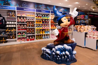 statue of Mickey mouse in sorcerer outfit with rows of soft toys behind blue signs with white writing above soft toys laminate floor