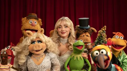 Sabrina Carpenter surrounded by Muppets, including Kermit the Frog, Miss Piggy and Fozzie Bear, in front of red curtains.