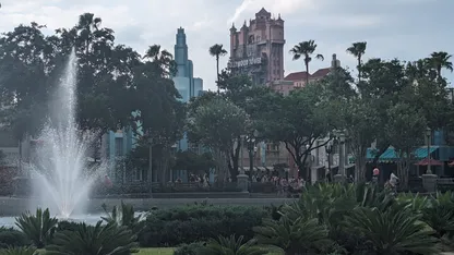 Fountain and landscaped gardens in front of Universal Studios’ Hollywood Tower attraction, with palm trees and buildings behind.