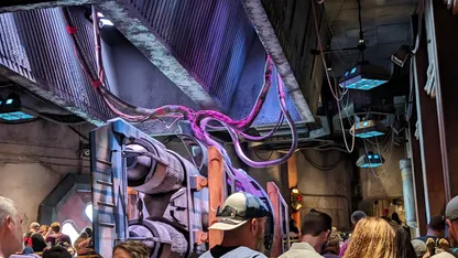 Themed industrial interior with purple tentacle-like cables, machinery, overhead lighting and visitors.