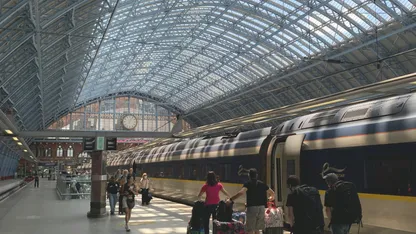Passengers board a train beneath the glass roof of a historic railway station.