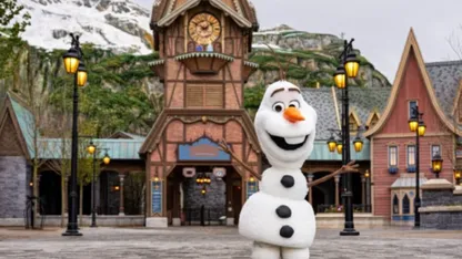 Olaf character standing in front of a clock tower and Nordic-style buildings in a snowy theme park.