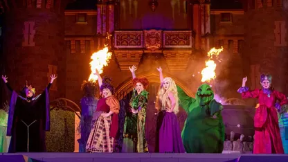 Stage performance featuring costumed actors, flames, and a green dragon-like character in a medieval castle setting.