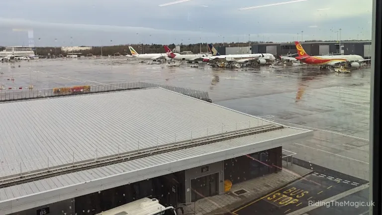 Airport apron with several parked aircraft on a wet tarmac, viewed from a terminal window.