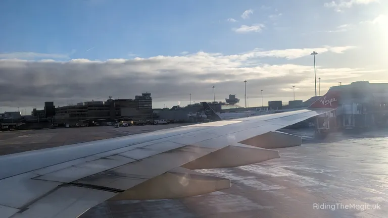 Aeroplane wing on the runway at an airport terminal with a Virgin aircraft in the background.