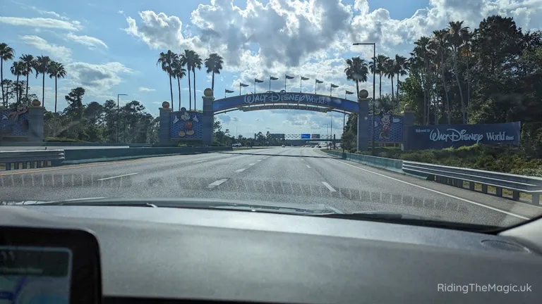 Car approaching the Walt Disney World entrance arch over a road.