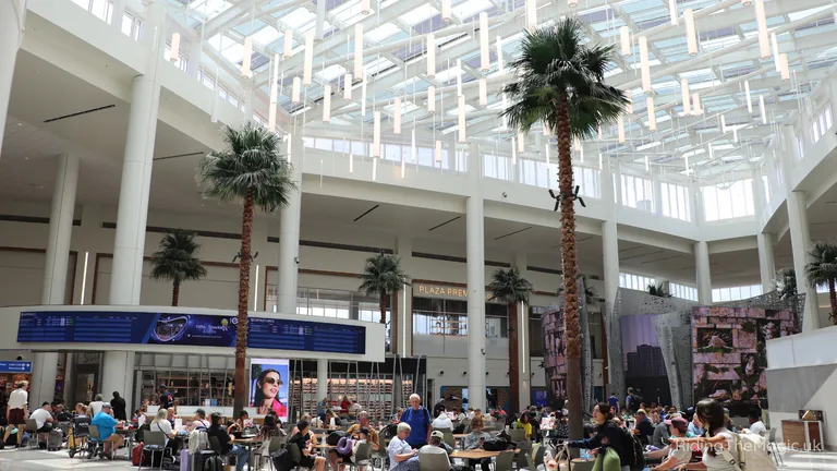 Indoor shopping mall atrium with palm trees, skylight and a busy food court.