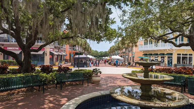 Tree-lined pedestrian shopping street with benches, fountain and market stalls