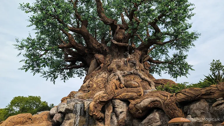 Large artificial tree with sprawling roots and waterfalls cascading over surrounding rocks.
