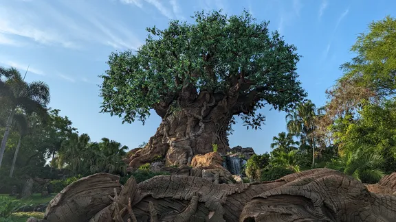 Large tree-like structure rising from rocky terrain, surrounded by lush greenery and a blue sky.