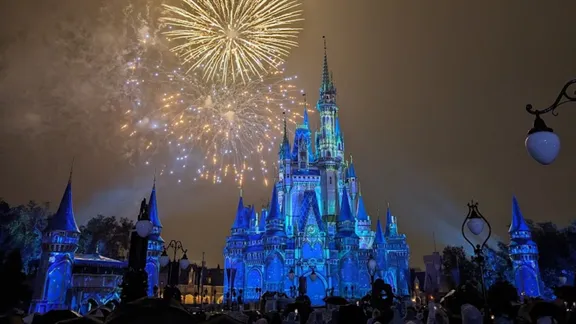 Cinderella Castle illuminated in blue beneath a fireworks display at night.