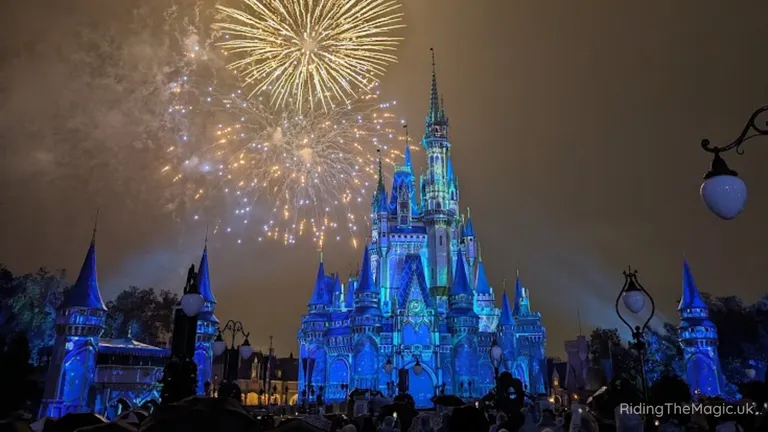 Cinderella Castle illuminated in blue beneath a fireworks display at night.