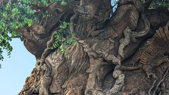 Intricately sculpted tree of life trunk covered with carved animal and human-like figures, twisting roots and foliage.