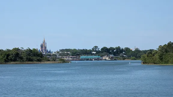 Seven Seas Lagoon with distant Cinderella castle on the horizon, framed by trees and blue sky.