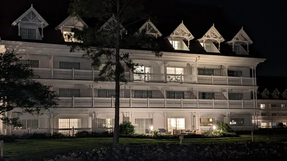Illuminated multi-storey building with white balconies and decorative gabled roof windows at night.
