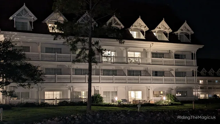 Illuminated multi-storey building with white balconies and decorative gabled roof windows at night.