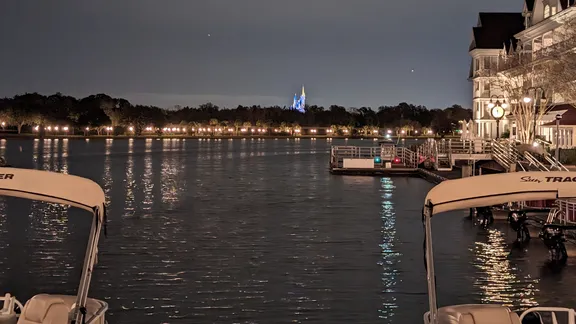 Night-time view across Seven Seas Lagoon, with boats in the foreground and a brightly lit Cinderella castle on the far shore.