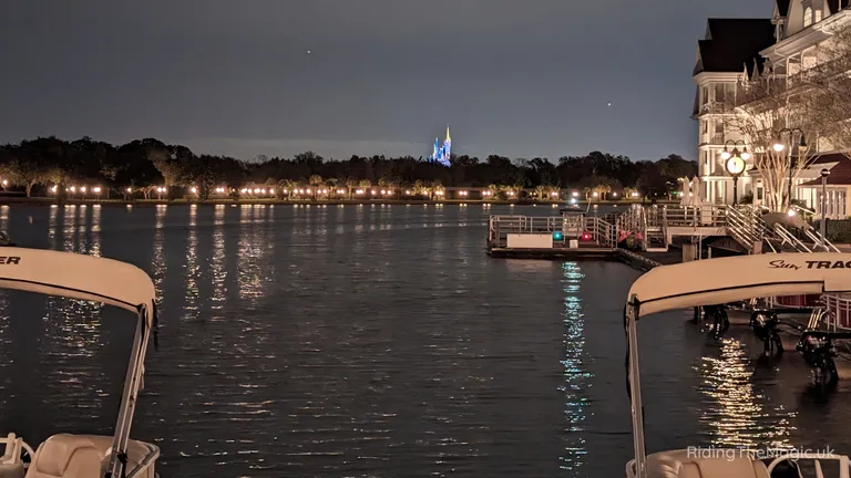 Night-time view across Seven Seas Lagoon, with boats in the foreground and a brightly lit Cinderella castle on the far shore.