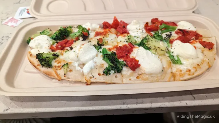 Flatbread pizza topped with mozzarella, tomatoes, broccoli and herbs in a takeaway container.