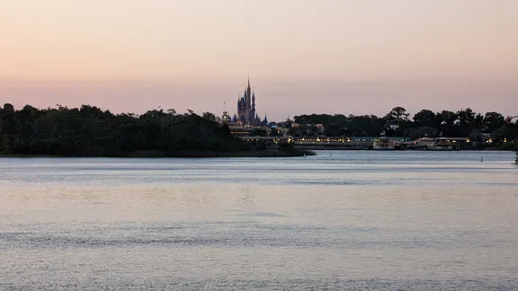 Cinderella Castle across the water at dusk, with trees along the shoreline.