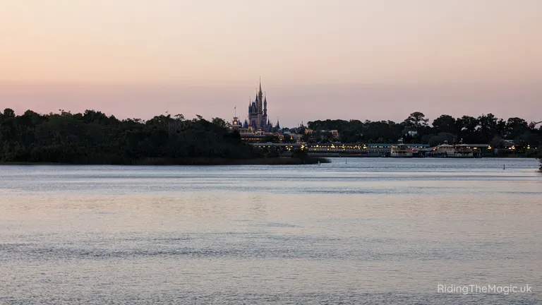 Cinderella Castle across the water at dusk, with trees along the shoreline.