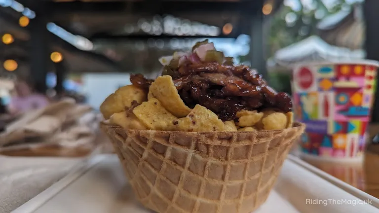Waffle cone filled with chips and topped with grilled meat and onions.