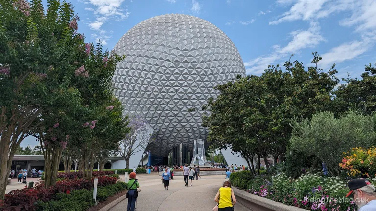 EPCOT’s geodesic Spaceship Earth sphere framed by trees and flowerbeds under a blue sky.