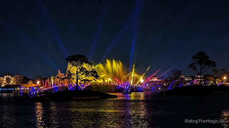 Night-time waterfront light and fountain display with colourful beams reflected on the water.