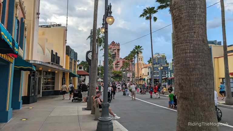 Pedestrian street lined with shops, palm trees, ornate street lamps and colourful Art Deco buildings, busy with people.