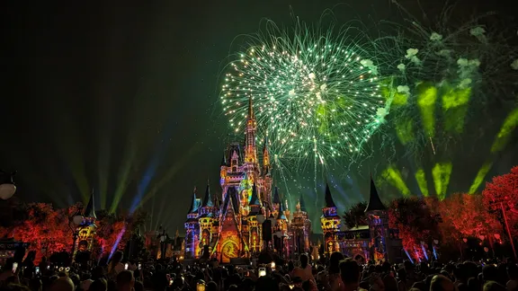 Illuminated fairytale castle with colourful projections and fireworks overhead at night.