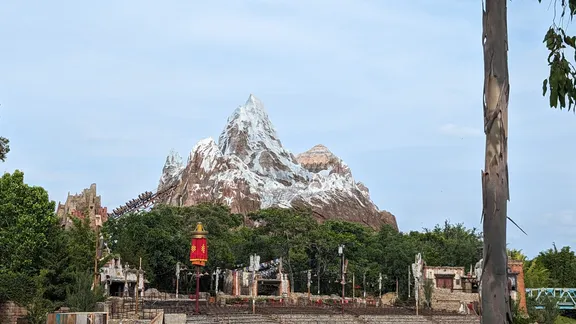 Snow-capped mountain-themed attraction behind a landscaped park with a red lantern and rustic temple structures.