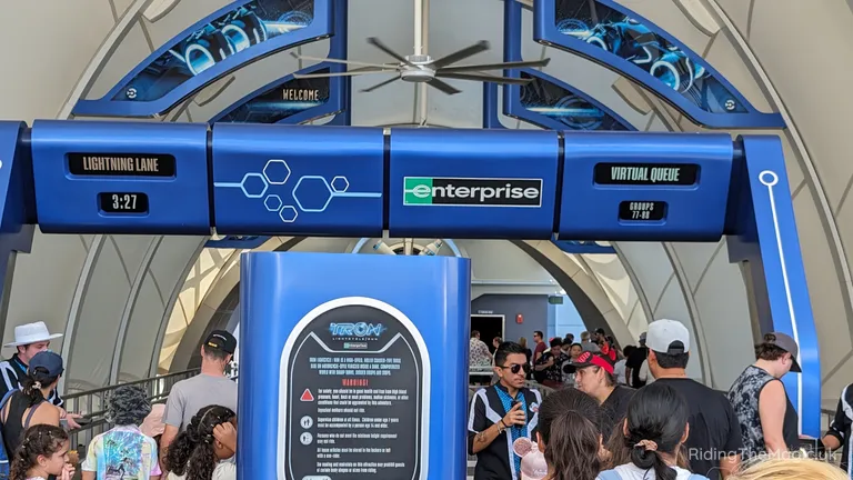 Crowds queue at a futuristic Magic Kingdom theme-park attraction TRON entrance with Lightning Lane and Virtual Queue signs.