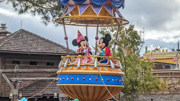 Mickey and Minnie Mouse wave from a colourful parade float at a theme park.
