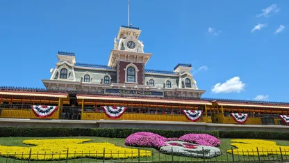 Walt Disney World’s Magic Kingdom entrance with an ornate railway station, bunting and colourful flower beds.