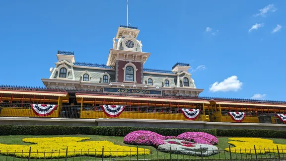 Walt Disney World’s Magic Kingdom entrance with an ornate railway station, bunting and colourful flower beds.