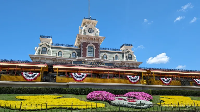 Walt Disney World’s Magic Kingdom entrance with an ornate railway station, bunting and colourful flower beds.