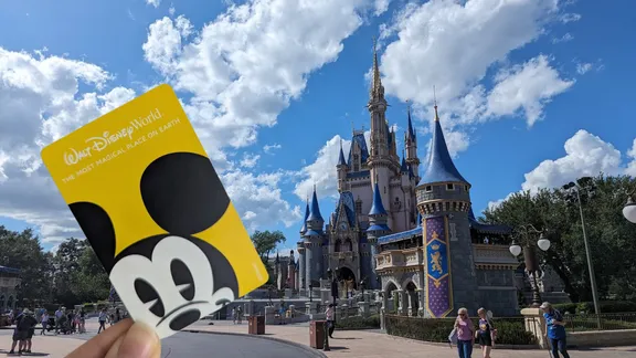 Hand holding a yellow Walt Disney World card featuring Mickey Mouse in front of Cinderella Castle under a blue sky.