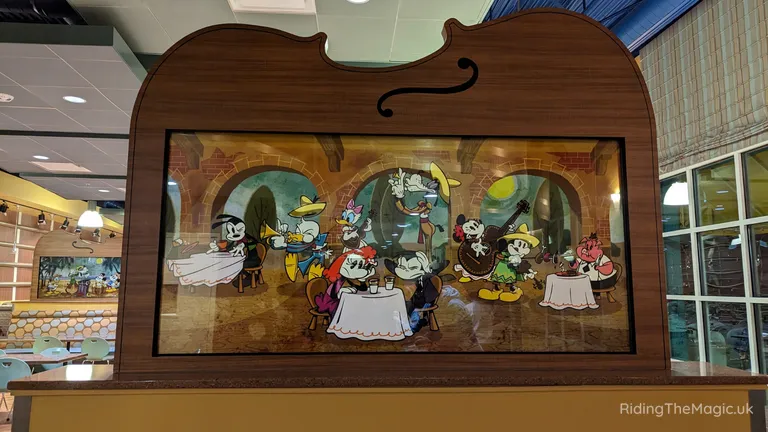 Disney cartoon characters gathered around dining tables in a display inside a wooden frame