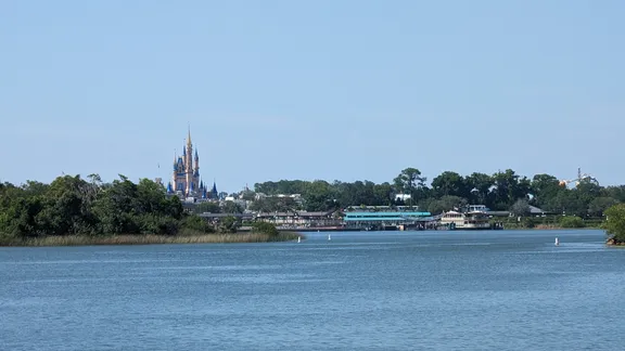 Lake in the foreground with a distant fairy-tale castle and shoreline buildings beneath a clear blue sky.